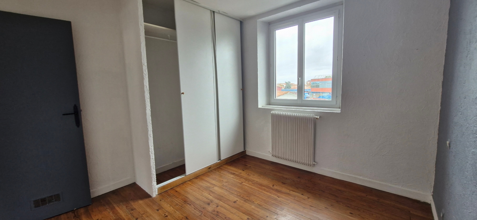 Ancienne chambre avant rénovation d'un appartement à Dax, avec parquet bois, placard intégré et fenêtre, dans un projet de transformation en colocation de 4 chambres.