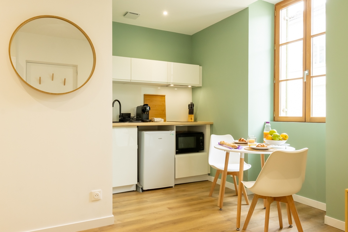 Pièce de vie avec cuisine ouverte et décoration vert sauge dans un appartement rénové à Dax